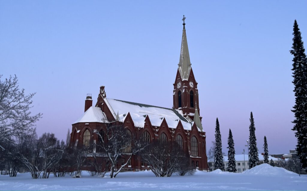 Image of Mikkeli's church in Finland covered in snow. The sky is glacial blue and the ground is also covered in snow.